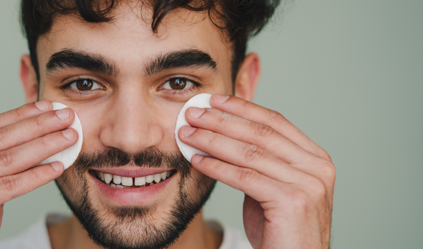 en smilende mann med skjegg som holder to peeling pads i ansiktet