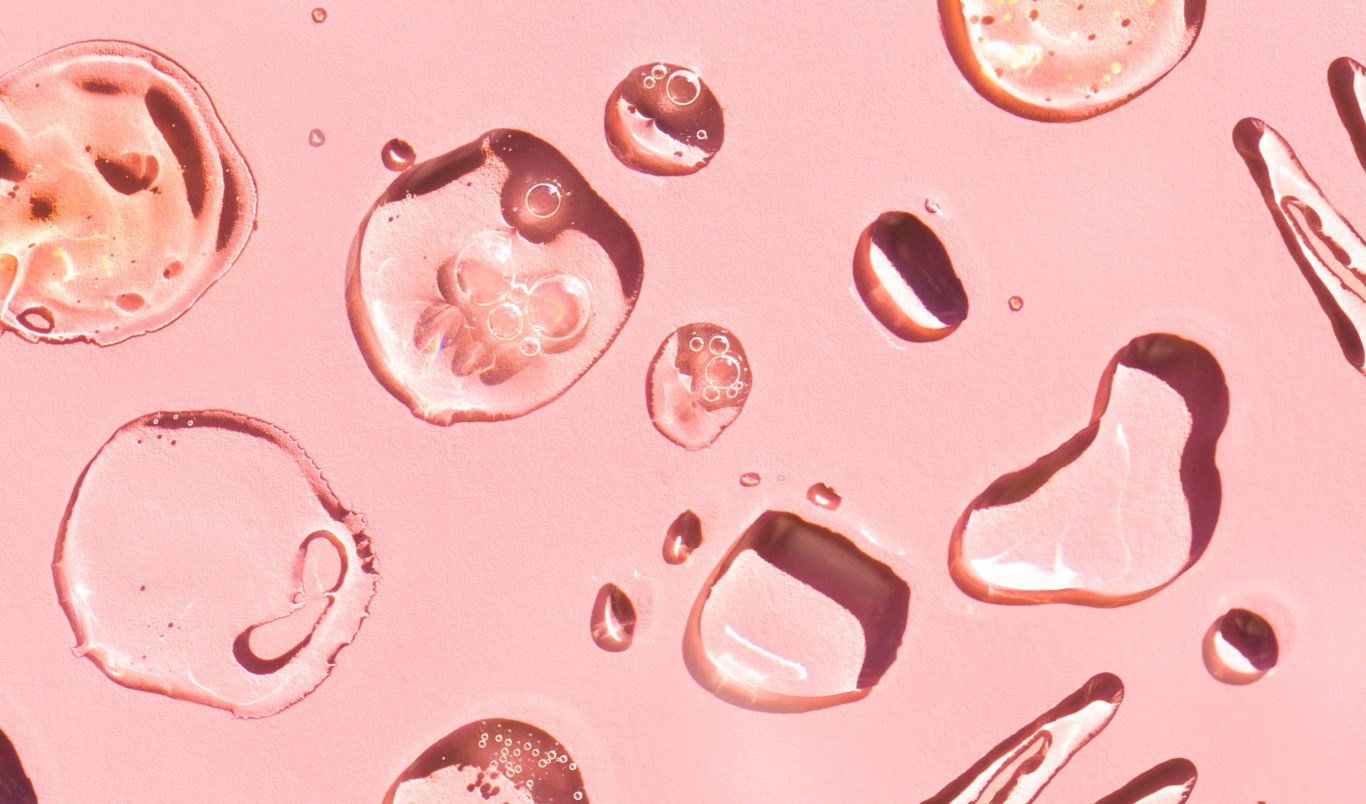 Nærbilde av gjennomsiktige dråper på en rosa overflate.
