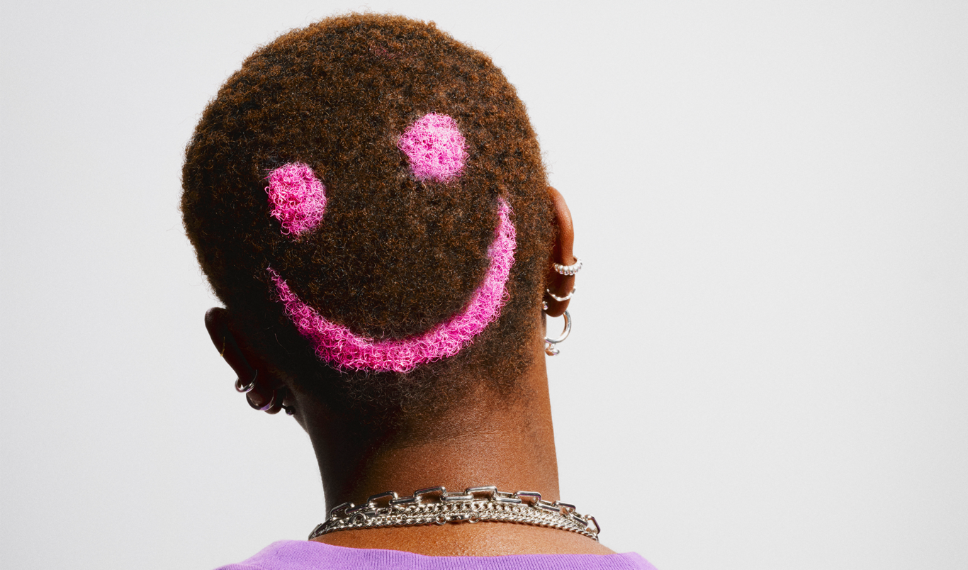 En person med kort hår har en rosa smiley ansiktsmålning på baksidan av huvudet.