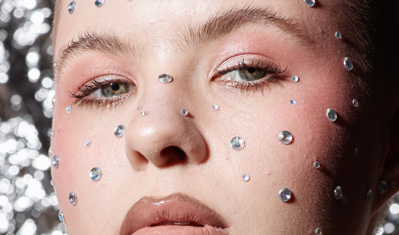 Kvinne med naturlig sminke, maskara og rhinestones rundt ansiktet som fregner.